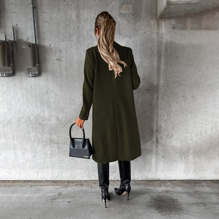 Vrouw in groene winterjas met zwarte laarzen en handtas, staand tegen een betonnen muur. Stijlvolle wintermode, trendy dameskleding.
